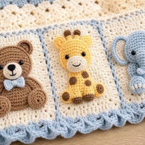 Puede incluir: Una manta de ganchillo color crema con un borde festoneado azul claro y aplicaciones tridimensionales de un oso marrón con pajarita azul claro, una jirafa amarilla con manchas marrones y un elefante azul claro con detalles en blanco.