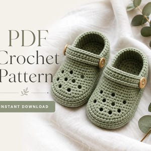 May include: A pair of sage green crocheted baby clogs featuring a perforated toe design and a functional heel strap secured with a small wooden button on each side. The text PDF Crochet Pattern and Instant Download is visible on the left.