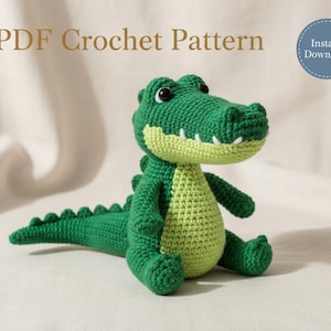 May include: A green and light green crocheted alligator toy with black eyes and white teeth. The text PDF Crochet Pattern and Instant Download are visible in the image. The alligator has a textured body with a long tail and small limbs.