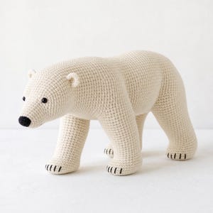 Può includere: Una statuetta di orso polare realizzata all'uncinetto a mano con filato color bianco sporco. L'orso presenta una superficie testurizzata, piccoli occhi a perla neri, un naso ricamato in nero e dettagli di artigli neri cuciti sulle quattro zampe.