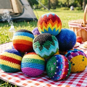 May include: A collection of spherical, crocheted yarn balls featuring various colorful patterns, including horizontal stripes, zig-zag designs, and solid hues in shades of red, orange, yellow, green, blue, purple, and black, arranged in a pile.