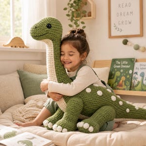May include: A large, green, crocheted dinosaur plush toy with a long neck, a cream-colored underbelly, and white circular spots along its back and tail. The dinosaur features black button eyes and textured, hand-stitched yarn detailing throughout.