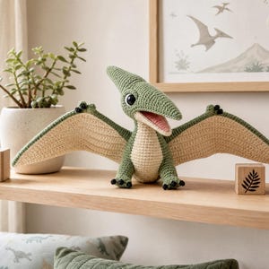 Peut inclure: Un jouet ptérodactyle au crochet avec un corps vert sauge, une poitrine et le dessous des ailes couleur crème, de grands yeux noirs et une bouche rose. Le dinosaure possède de petites griffes noires aux pieds et aux ailes, avec une crête pointue.