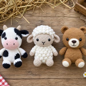 May include: Three handmade crochet stuffed animals including a black and white cow with a pink snout, a cream-colored sheep with a textured woolly body, and a brown bear with a white muzzle, all featuring black safety eyes and stitched details.