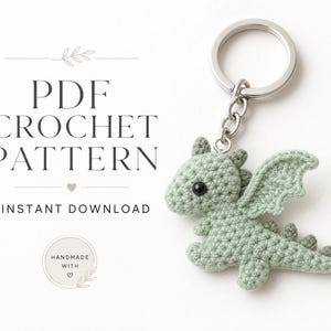 Op de afbeelding: Een lichtgroene gehaakte draak sleutelhanger met zwarte kraaloogjes, bevestigd aan een zilveren metalen ring. De tekst luidt: PDF CROCHET PATTERN, INSTANT DOWNLOAD, HANDMADE WITH.