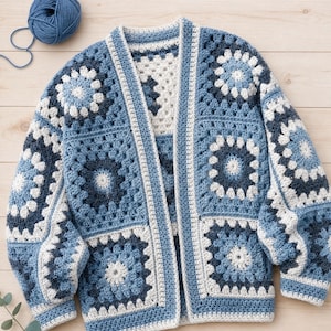 Può includere: Un cardigan a maniche lunghe realizzato con diversi quadrati all'uncinetto in tonalità blu navy, blu medio e bianco sporco. Il capo presenta un motivo geometrico floreale ripetuto e un bordo a coste solido lungo la parte anteriore.