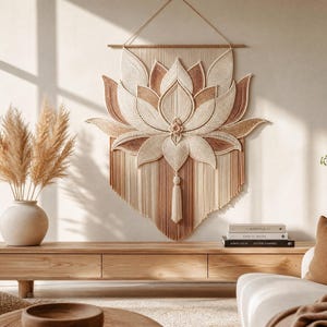 May include: A large macrame wall hanging featuring a lotus flower design in cream and terracotta tones. The piece is constructed from knotted cord, suspended from a wooden dowel with a string, and includes a central tassel at the bottom edge.