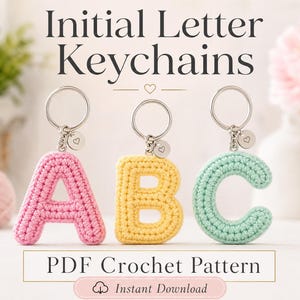 以下が含まれることがあります： ピンク、イエロー、ミントグリーンの3つのクロッシェ編みの文字キーホルダー。それぞれにシルバーの金属リングとハートが刻印された小さな円形のチャームが付いています。Initial Letter KeychainsおよびPDF Crochet Patternというテキストが表示されています。