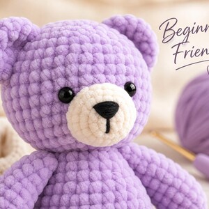 Op de afbeelding: Een lavendelkleurige gehaakte teddybeer met een crèmekleurige snuit, zwarte plastic ogen en een zwart geborduurde neus. De tekst "Beginner Friendly" met een klein hartje is rechtsboven zichtbaar, naast een bol lavendelkleurig garen.