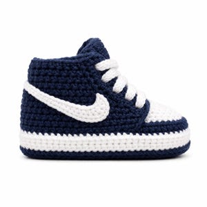 Peut inclure: Une basket montante fabriquée en fil bleu marine et blanc selon une technique de crochet. La chaussure présente un accent blanc en forme de virgule sur le côté, des lacets blancs, un bout blanc et une épaisse semelle blanche sur une base marine.