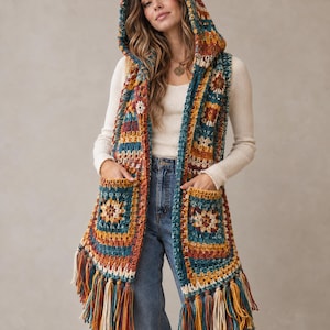 May include: A sleeveless hooded vest crafted from multicolored crochet yarn in shades of teal, mustard yellow, rust orange, and cream. The garment features square granny motifs, two front patch pockets, and long fringe trim along the hem.