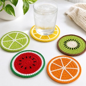 Può includere: Un set di cinque sottobicchieri rotondi all'uncinetto con disegni di frutta, tra cui lime, limone, kiwi, anguria e arancia. Un sottobicchiere sostiene un bicchiere trasparente riempito con acqua e cubetti di ghiaccio.