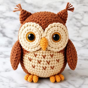 Puede incluir: Un juguete de peluche de búho tejido a ganchillo en color marrón y crema, con grandes ojos de plástico negro, un pico amarillo y pequeños mechones de hilo en la parte superior de la cabeza. El pecho es crema con puntadas bordadas en forma de V.