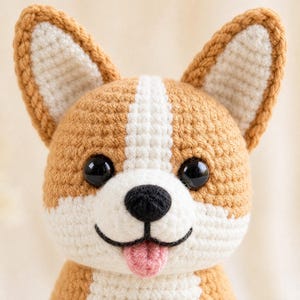 Può includere: Un peluche all'uncinetto a forma di cane Corgi. Il giocattolo è realizzato in filato color marrone chiaro e bianco, con grandi occhi in plastica nera, un naso ricamato nero e una piccola lingua rosa che sporge da una bocca cucita.