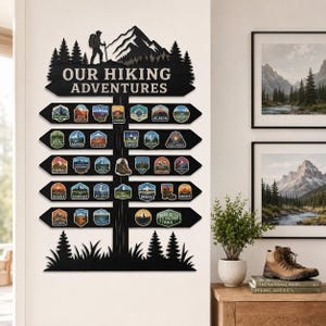 May include: A black wall-mounted sign titled "OUR HIKING ADVENTURES" featuring a silhouette of a hiker and mountains at the top. The sign has five horizontal arrow-shaped boards displaying various colorful national park patches and hiking icons.