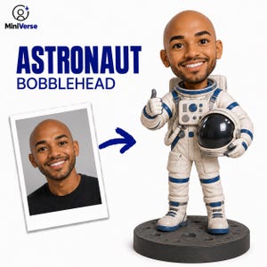 Könnte beinhalten: Eine personalisierte Wackelfigur einer glatzköpfigen Person mit Bart, die einen weiß-blauen Astronautenanzug trägt, einen Helm unter dem Arm hält und den Daumen hebt. Die Figur steht auf einem dunkelgrauen, runden Sockel mit Krater-Optik.