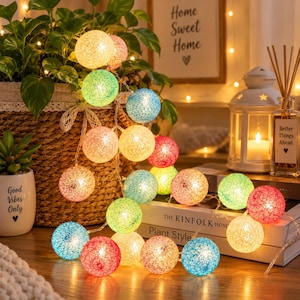 Puede incluir: Una guirnalda de luces LED decorativas con pantallas esféricas hechas de hilo tejido en varios colores, incluyendo rojo, azul, verde, amarillo y rosa. Las esferas iluminadas están dispuestas en racimo, creando un brillo cálido.