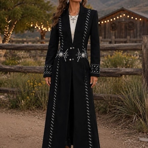 May include: A long black coat featuring a notched lapel, long sleeves, and a front button closure. The coat is decorated with vertical rows of silver-toned studs and circular metal embellishments at the waist, paired with brown ankle boots.