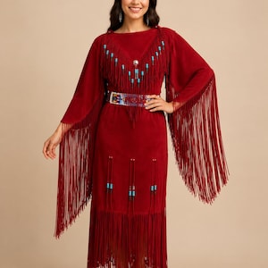 May include: A deep red suede dress featuring long, flowing fringe along the sleeves and hem. The garment is accented with turquoise and black beadwork on the chest and skirt, and includes a wide, multicolored beaded belt at the waist.