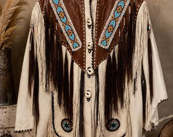 May include: A cream-colored jacket featuring brown leather panels on the chest, adorned with intricate blue, orange, and white beadwork. The garment includes long cream and dark brown fringe detailing, a collared neckline, and round white buttons.