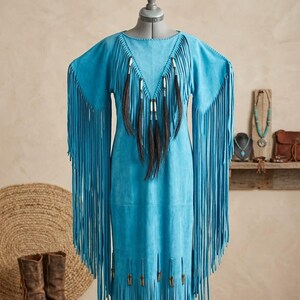 May include: A bright turquoise suede dress featuring long, flowing fringe along the sleeves and hem. The bodice is decorated with a V-shaped arrangement of dark brown horsehair tassels secured with silver-toned metal beads and accents.