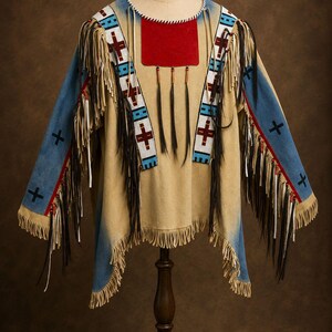 May include: A tan suede shirt featuring long fringe along the sleeves and hem, blue panels on the sleeves with black cross symbols, a red chest patch, and beaded shoulder strips with red and blue geometric patterns and hanging black feathers.
