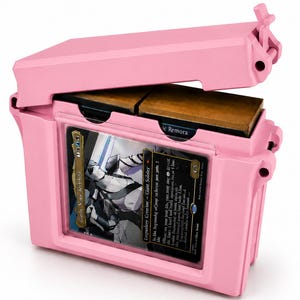May include: A light pink plastic storage case with a hinged lid, featuring a clear front window displaying a trading card titled Gorrin Nokie Aeteteist. The interior contains two stacks of cards, with one card partially visible labeled Mystic Remora.