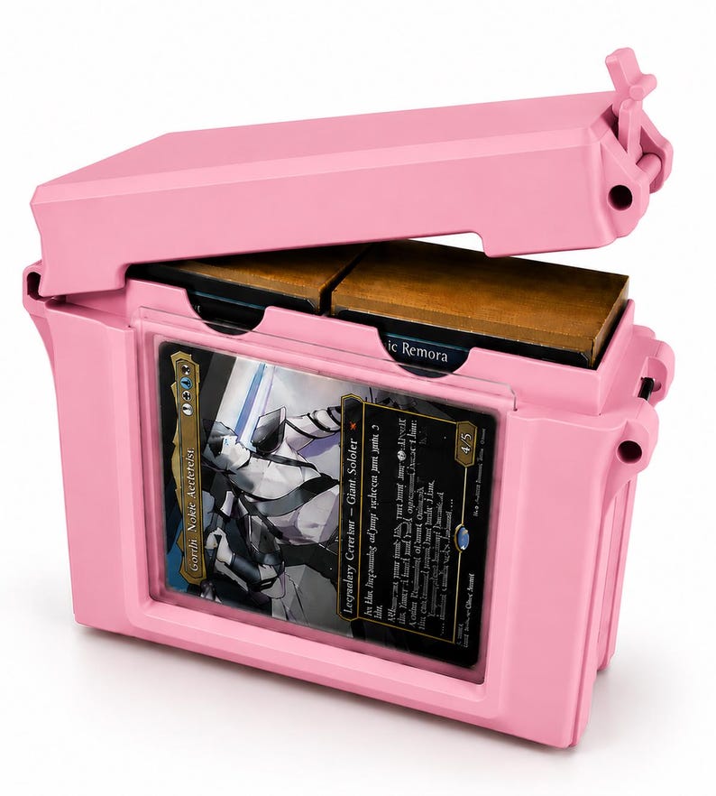 May include: A light pink plastic storage case with a hinged lid, featuring a clear front window displaying a trading card titled Gorrin Nokie Aeteteist. The interior contains two stacks of cards, with one card partially visible labeled Mystic Remora.