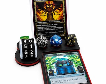 May include: A black and red gaming display stand featuring a vertical slot for a trading card, a horizontal slot for a second card, and three circular indentations holding a black and white life counter dial and three multi-sided dice.