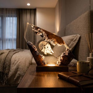 Puede incluir: Una lámpara decorativa que presenta un bloque de resina transparente con bordes de madera natural incrustados y un modelo en miniatura de la nave Millennium Falcon en su interior. Montada sobre una base de madera con luz integrada.