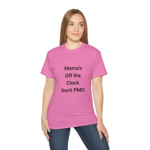 May include: A bright pink short-sleeved t-shirt featuring black text printed on the front that reads: Mama's Off the Clock Don't PMO. The garment has a classic crew neckline and a straight hem, providing a simple and standard fit for casual wear.