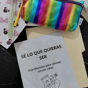 Puede incluir: Un estuche metálico de colores arcoíris con cremallera, una varita de burbujas y un libro para colorear titulado SÉ LO QUE QUIERAS SER 10 profesiones para colorear versión niñas con una ilustración de líneas y el hashtag #mamáingenieramx en la portada.
