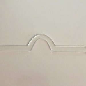 May include: A clear, flat, acrylic template piece featuring a central arched bridge section flanked by two straight horizontal arms, each ending in a small circular tab with a centered hole for alignment or attachment purposes.