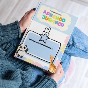 Puede incluir: Un libro de tapa dura titulado Pequeños Genios Aprendo Jugando con una cubierta azul claro que presenta un panda, una jirafa, un clip en forma de estrella y el texto Este Cuaderno Pertenece A para escribir un nombre.