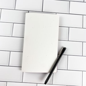 Closed Traveler's Notebook insert showing the speckled white card stock cover with colored inside paper visible along the page edges. Saddle-stitched booklet made in the USA by Emiline and Jayne. Physical paper insert only, notebook cover and accessories not included.