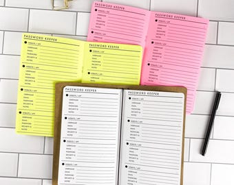 May include: Three open password keeper booklets in neon yellow, bright pink, and brown with white pages. Each booklet features printed lines for website, app, username, email, password, security question, and notes. A gold binder clip and black pen.