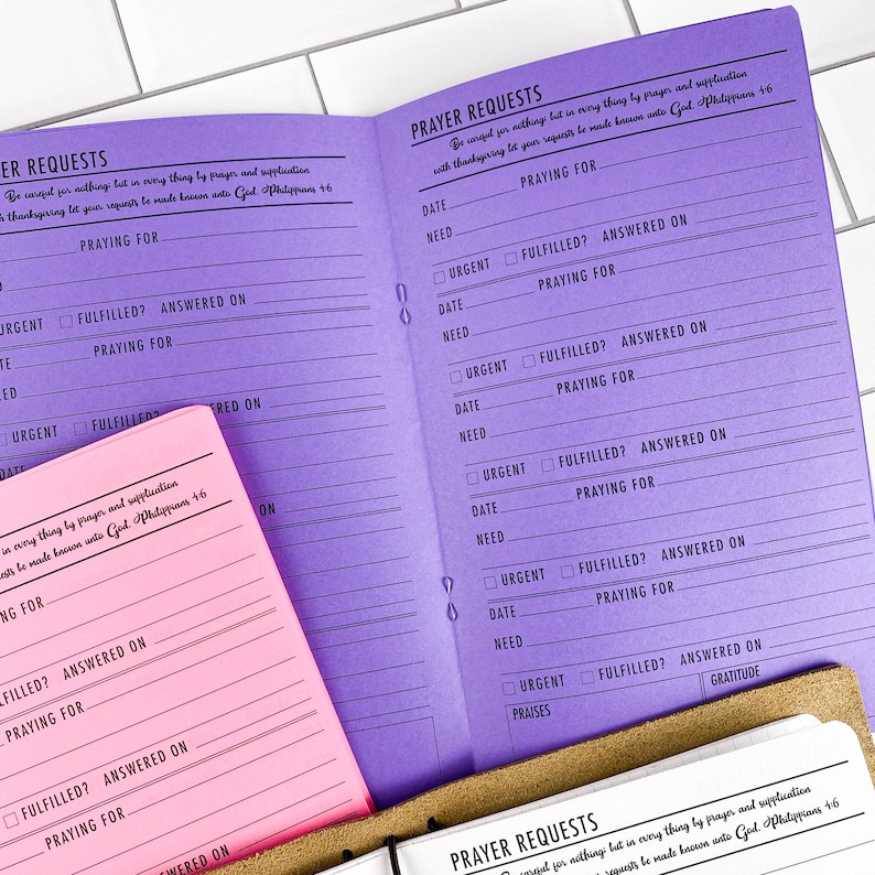 Prayer requests traveler's notebook insert shown in Bubblegum pink and Violet Sky purple paper versions on white subway tile, displaying the prayer journal layout with Philippians 4:6 verse and tracking fields. Made in the USA by Emiline and Jayne. Physical paper insert only, notebook cover and accessories not included.