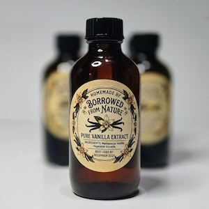 May include: A brown glass bottle with a black cap containing pure vanilla extract. The oval label features the text "Homemade by Borrowed from Nature," "Pure Vanilla Extract," ingredients, and a "Best Used by December 2029" date.