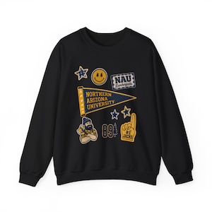 May include: A black crewneck sweatshirt featuring a collection of patches including a pennant that reads Northern Arizona University, a smiley face, a lumberjack character, the number 89, a foam finger labeled #1 Jacks, and various stars.