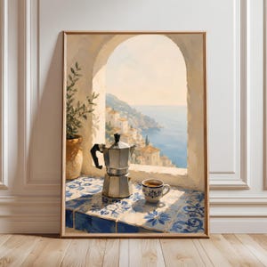 Puede incluir: Una lámina de arte enmarcada que muestra una cafetera italiana de plata y una pequeña taza de cerámica sobre una superficie de azulejos azules y blancos. La escena se sitúa en una ventana arqueada con vistas a una ciudad costera.