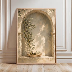 May include: A framed wall art print depicting an arched stone alcove with a hanging olive branch and a shallow bowl filled with green and black olives. The scene features soft, dappled sunlight and shadows cast against a textured, neutral-toned wall.