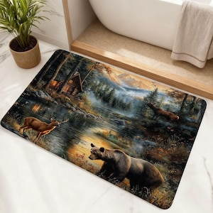 May include: A rectangular bath mat featuring a detailed nature scene with a brown bear in the foreground, a deer standing near a reflective lake, and a rustic wooden cabin nestled among pine trees under a misty mountain landscape.