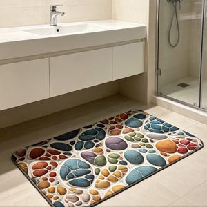May include: A rectangular bathroom rug featuring a repeating pattern of rounded, pebble-like shapes in various colors including blue, orange, purple, green, and brown, separated by a light-colored, textured grid-like border with rounded edges.