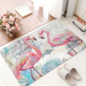 May include: A rectangular floor mat featuring a watercolor-style illustration of two pink flamingos facing each other. The background includes abstract splashes of blue, teal, and white, with subtle seashell and aquatic patterns integrated throughout.