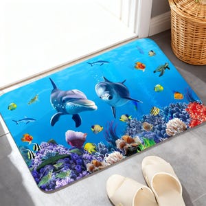 May include: A rectangular floor mat featuring a vibrant underwater scene with two large grey dolphins swimming in clear blue water above a colorful coral reef filled with various small tropical fish, including yellow, orange, and striped species.
