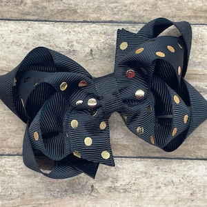 May include: A black hair bow with gold polka dots. The bow is made of grosgrain ribbon and is tied in a large, fluffy knot.