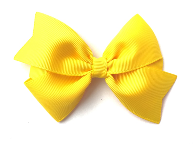 Pode incluir: Um la&ccedil;o amarelo brilhante feito de fita de grosgrain. O la&ccedil;o &eacute; amarrado em um estilo cl&aacute;ssico com duas voltas e um n&oacute; central.