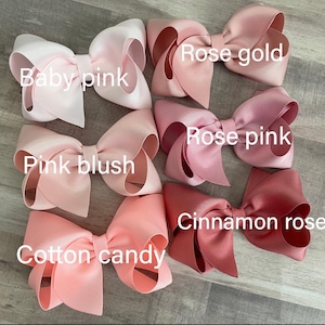 K&ouml;nnte beinhalten: Eine Sammlung handgefertigter Haarschleifen in verschiedenen Rosat&ouml;nen, darunter Babyrosa, Pink Blush, Zuckerwatte, Ros&eacute;gold, Rosenrosa und Zimtrose. Jede Schleife ist mit ihrem Farbnamen beschriftet.