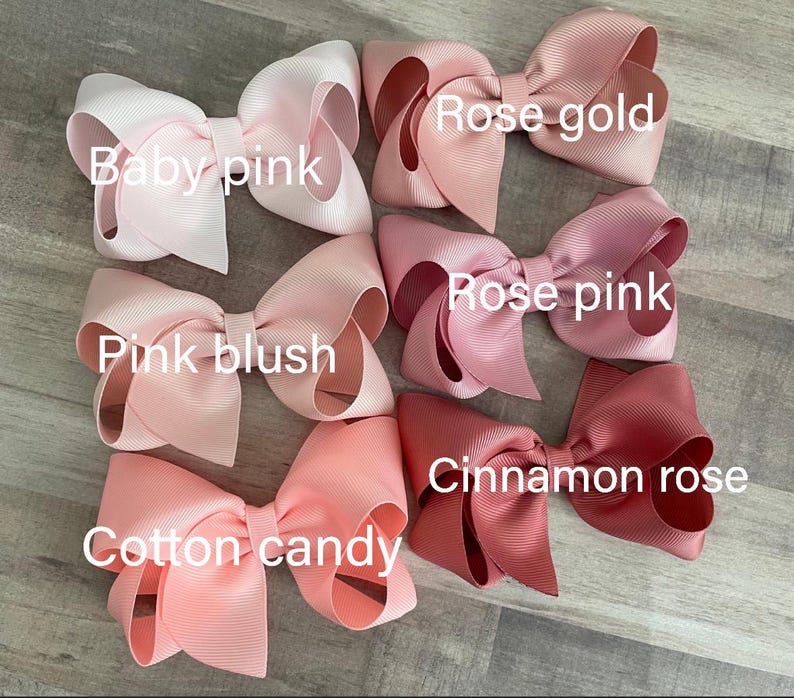 K&ouml;nnte beinhalten: Eine Sammlung handgefertigter Haarschleifen in verschiedenen Rosat&ouml;nen, darunter Babyrosa, Pink Blush, Zuckerwatte, Ros&eacute;gold, Rosenrosa und Zimtrose. Jede Schleife ist mit ihrem Farbnamen beschriftet.