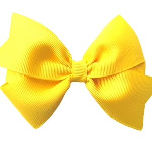Pode incluir: Um la&ccedil;o amarelo brilhante feito de fita de grosgrain. O la&ccedil;o &eacute; amarrado em um estilo cl&aacute;ssico com duas voltas e um n&oacute; central.